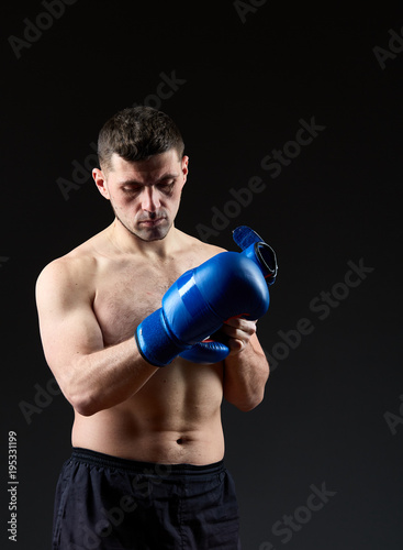 Low key studio portrait of handsome muscular fighter preparing for boxing on dark blurred background © Aleksey