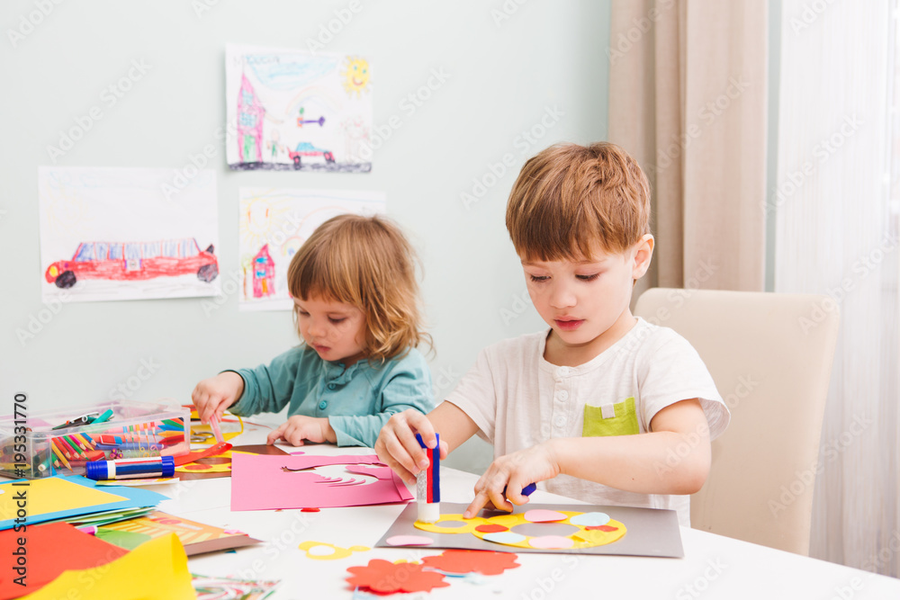 Fototapeta premium Happy cheerful children drawing in paper using a lot of painting tools sitting at a table. 