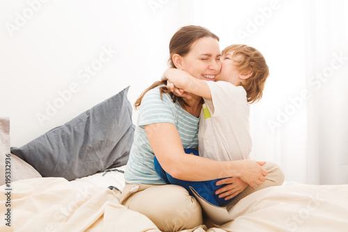 little son is hugging and kissing her mom and relaxing and playing in the bed at the weekend together, lazy morning. Mother's day.