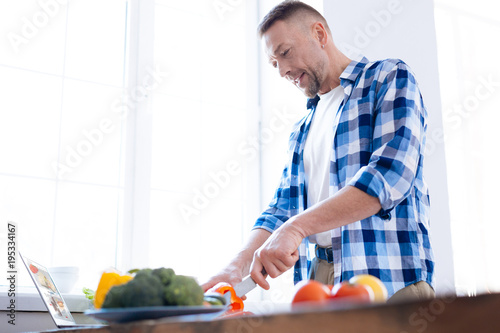 Food is fuel. Pleasant glad focused man holding knife for chopping salad and consuming vegetables
