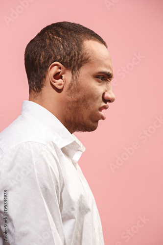 The young emotional angry man screaming on pink studio background