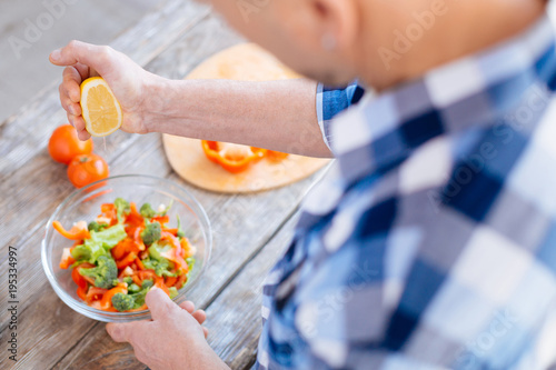 Eat fewer calories. Selective focus of transparent bowl placing on wooden surface where vegetables put and male hand squeezing fresh lemon