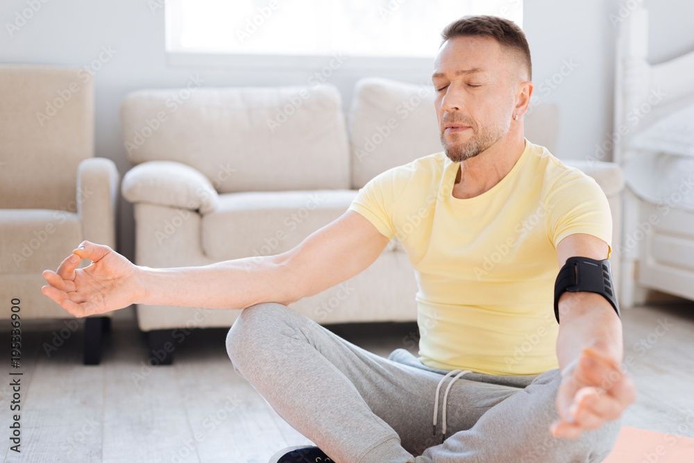 Inner tranquility. Thoughtful nice pleased man practicing meditation while closing eyes and posing on floor Inner tranquility. Thoughtful nice pleased man practicing meditation while closing eyes and posing on floor