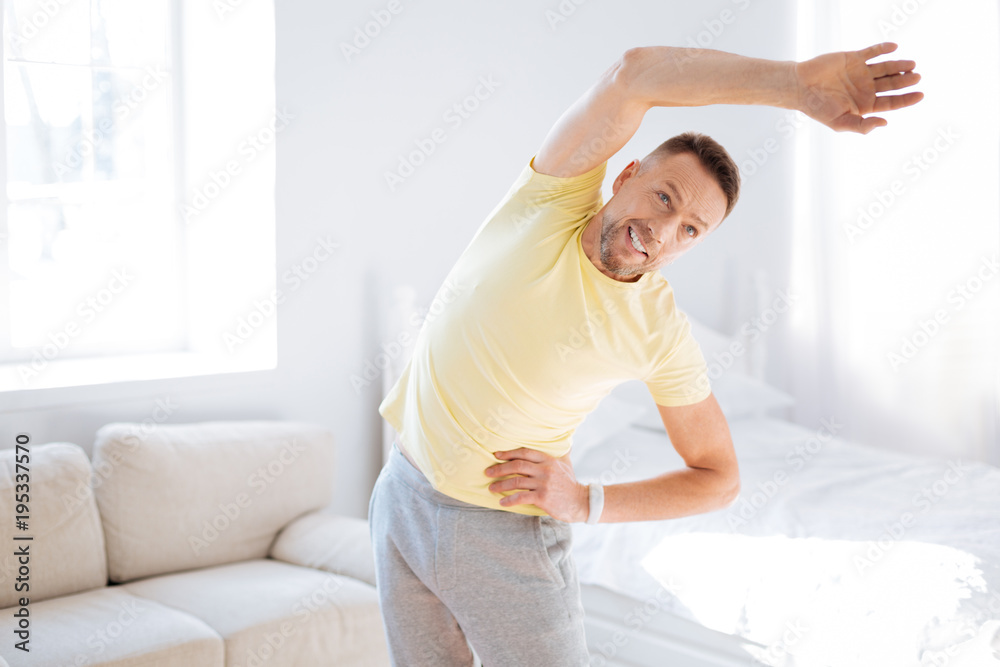 Biohacks for spine. Charming nice pleased man tilting to right while elevating hand and grinning Biohacks for spine. Charming nice pleased man tilting to right while elevating hand and grinning