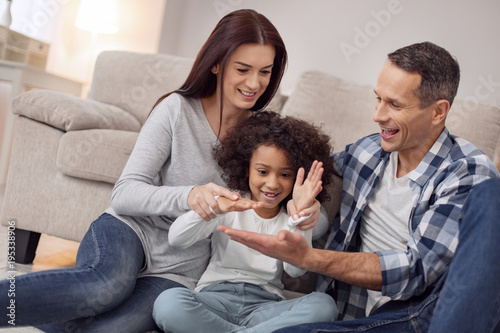 Inspired family. Pretty inspired curly-haired smiling and having fun with her parents while they all sitting on the floor photo
