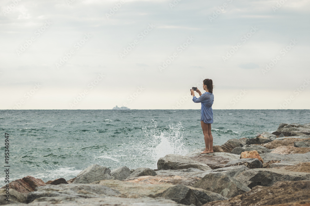 young woman taking photos of a ship in the ocean on her smartphone. travel smartphonography