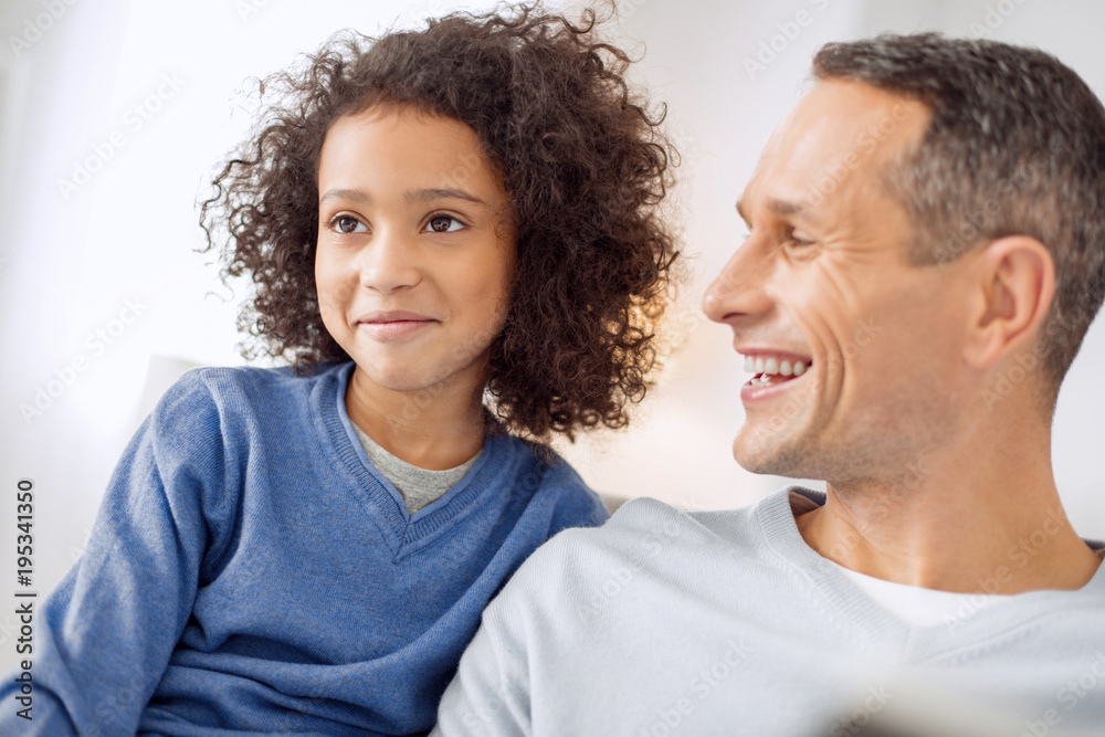 Joking. Handsome alert dark-haired smiling and looking at his daughter while sitting together Joking. Handsome alert dark-haired smiling and looking at his daughter while sitting together