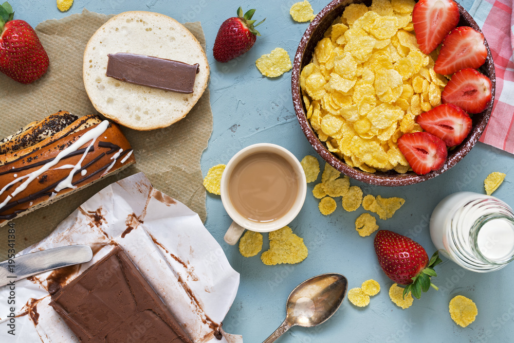 Breakfast, corn flakes with fresh strawberries and milk, chocolate butter with fresh pastries on a gray background. View from above. Breakfast, corn flakes with fresh strawberries and milk, chocolate butter with fresh pastries on a gray background. View from above.