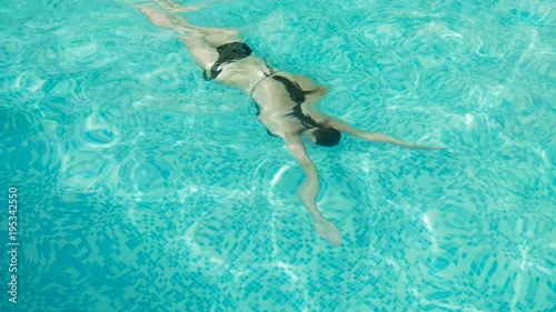 girl swims in the outdoor pool at the hotel in a black swimsuit