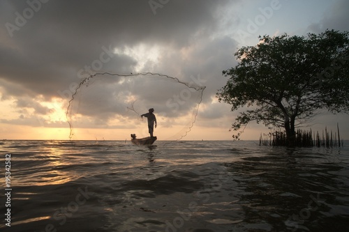 Silhouette of Fishermen throwing net fish on sunset time in a lake.