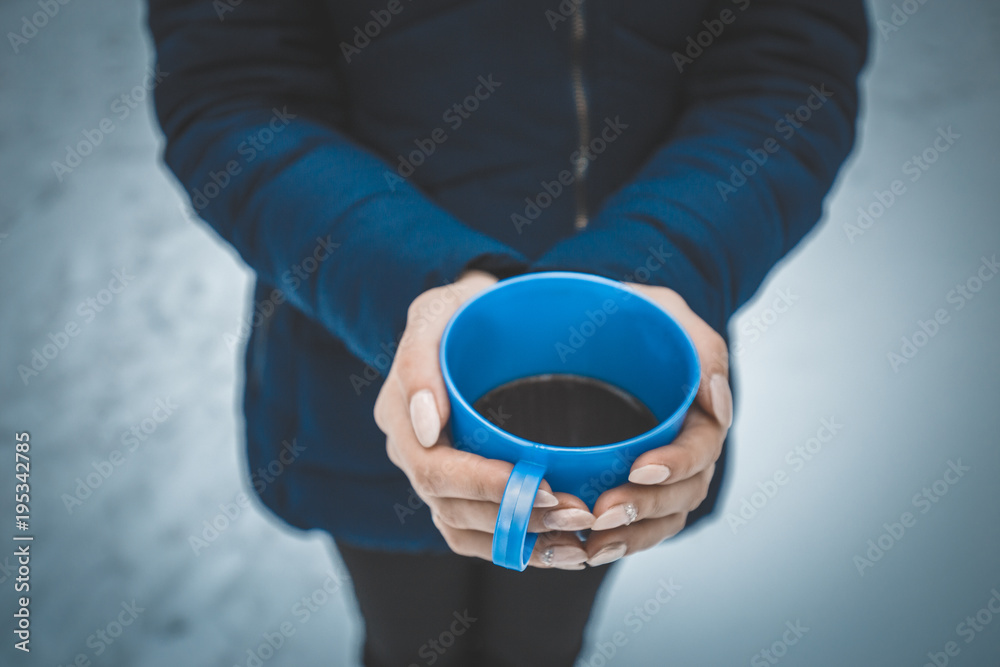 The girl warms her hands about a Cup of tea or coffee in the winter outdoors in the Park for a walk The girl warms her hands about a Cup of tea or coffee in the winter outdoors in the Park for a walk