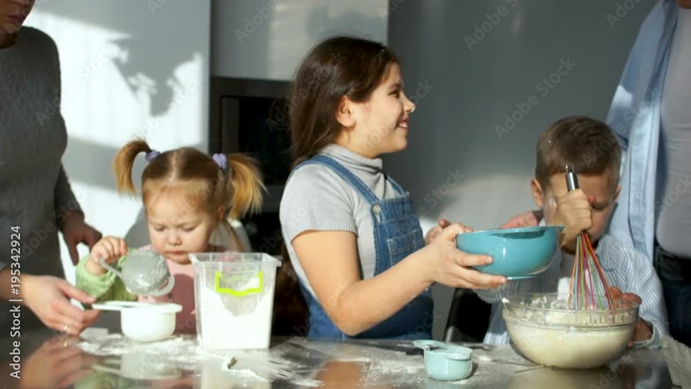 The whole family in the kitchen is preparing food. The eldest daughter stained her father with flour. Children's joke. Three children The whole family in the kitchen is preparing food. The eldest daughter stained her father with flour. Children's joke. Three children