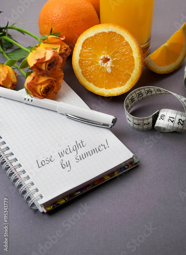 Oranges, orange roses, Notepad and pen on grey background. A place for a label