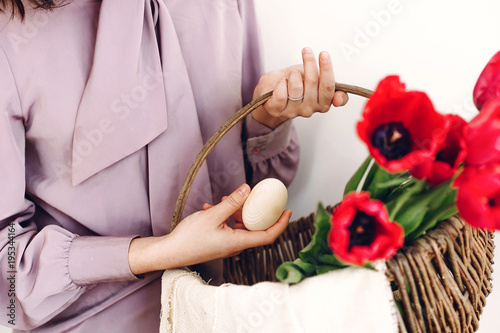 easter hunt concept. beautiful stylish girl holding basket with pink tulips and natural easter eggs on white background isolated. happy child looking for egg. space for text