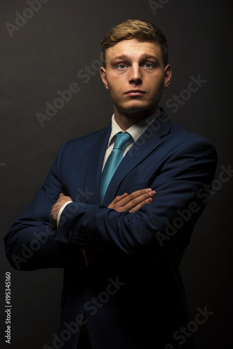 Businessman in suit over dark background, crossed arms, portrait. © Wisiel
