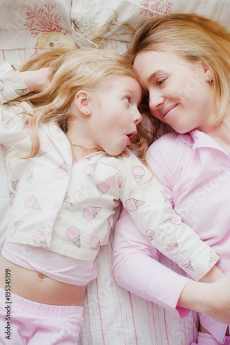 mother and daughter lying on bed in pink pajamas