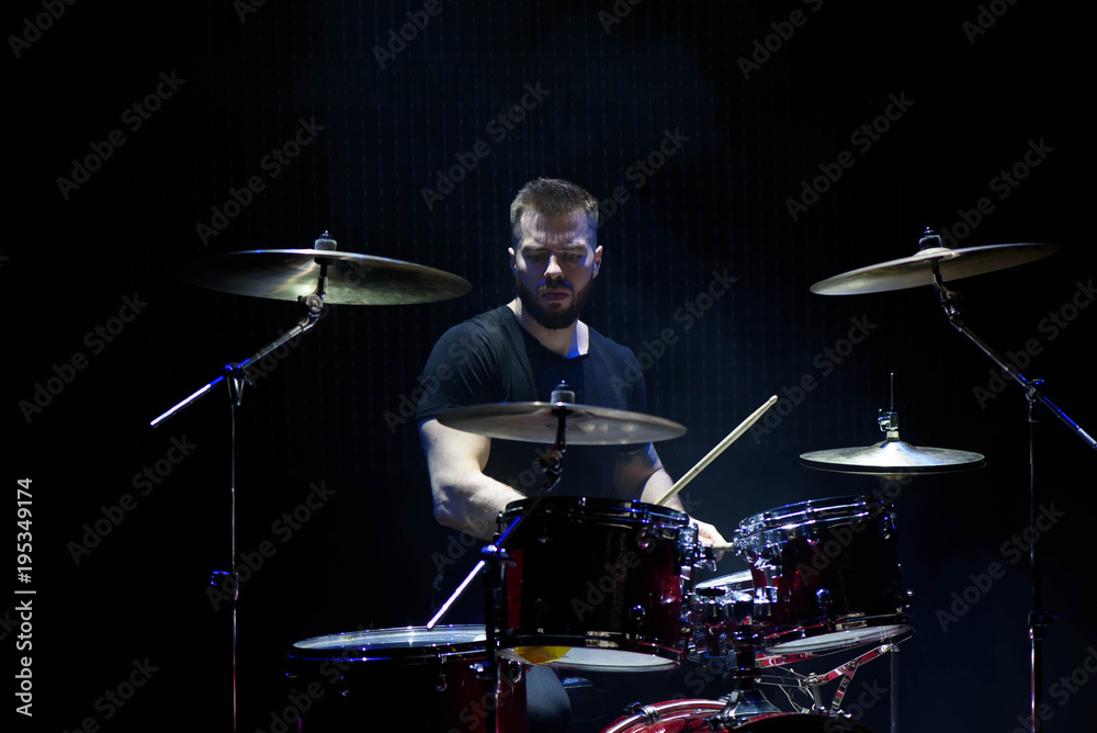 Fototapeta premium Drummer in a cap and headphones plays drums at a concert under white light in a smoke