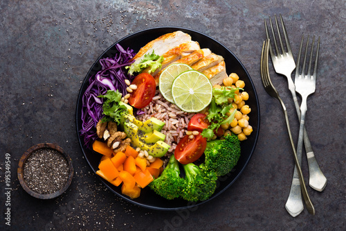 Buddha bowl dish with chicken fillet, brown rice, avocado, pepper, tomato, broccoli, red cabbage, chickpea, fresh lettuce salad, pine nuts and walnuts. Healthy balanced eating. Top view