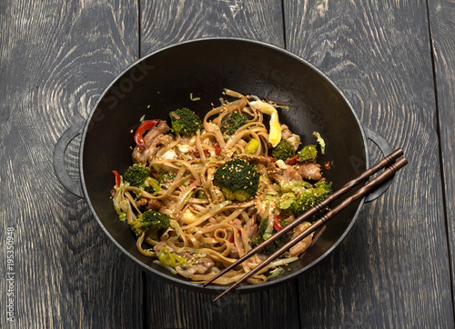 Asian dish of meat, vegetables and noodles with spices in wok, on background of table