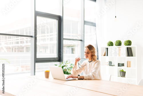 Happy young business woman sitting in office using laptop