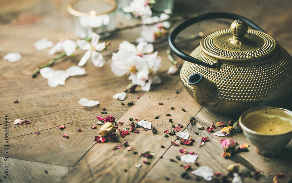 Traditional Asian tea ceremony arrangement. Iron teapot, cups, blooming almond flowers, dried rose buds and candles over wooden table background, selective focus, copy space - obrazy, fototapety, plakaty 