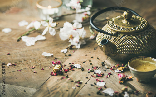 Traditional Asian tea ceremony arrangement. Iron teapot, cups, blooming almond flowers, dried rose buds and candles over wooden table background, selective focus, copy space