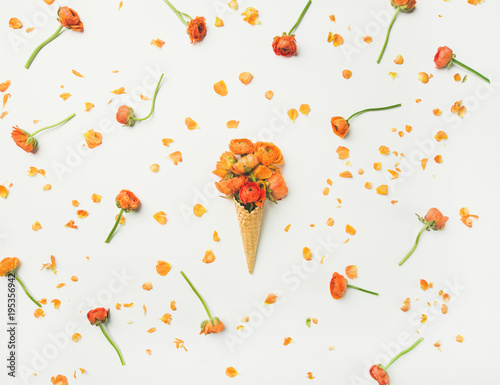 Flat-lay of waffle sweet cone with orange buttercup flowers over white background, top view. Spring or summer mood concept
