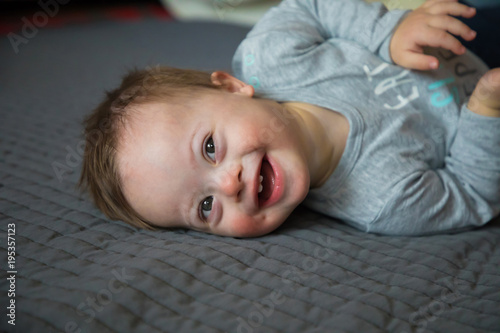 Portrait of cute baby boy with Down syndrome on the bed in home bedroom photo