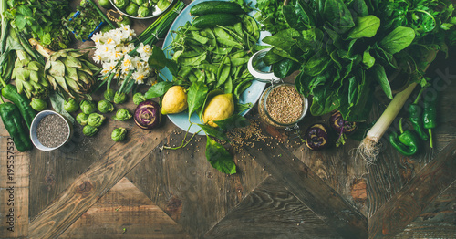 Spring healthy vegan food cooking ingredients. Flat-lay of vegetables, fruit, seeds, sprouts, flowers, greens over wooden background, top view, copy space, wide composition. Diet food concept