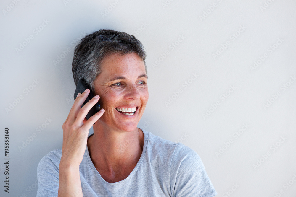 Close up beautiful middle age woman smiling and talking on mobile phone against white wall Close up beautiful middle age woman smiling and talking on mobile phone against white wall
