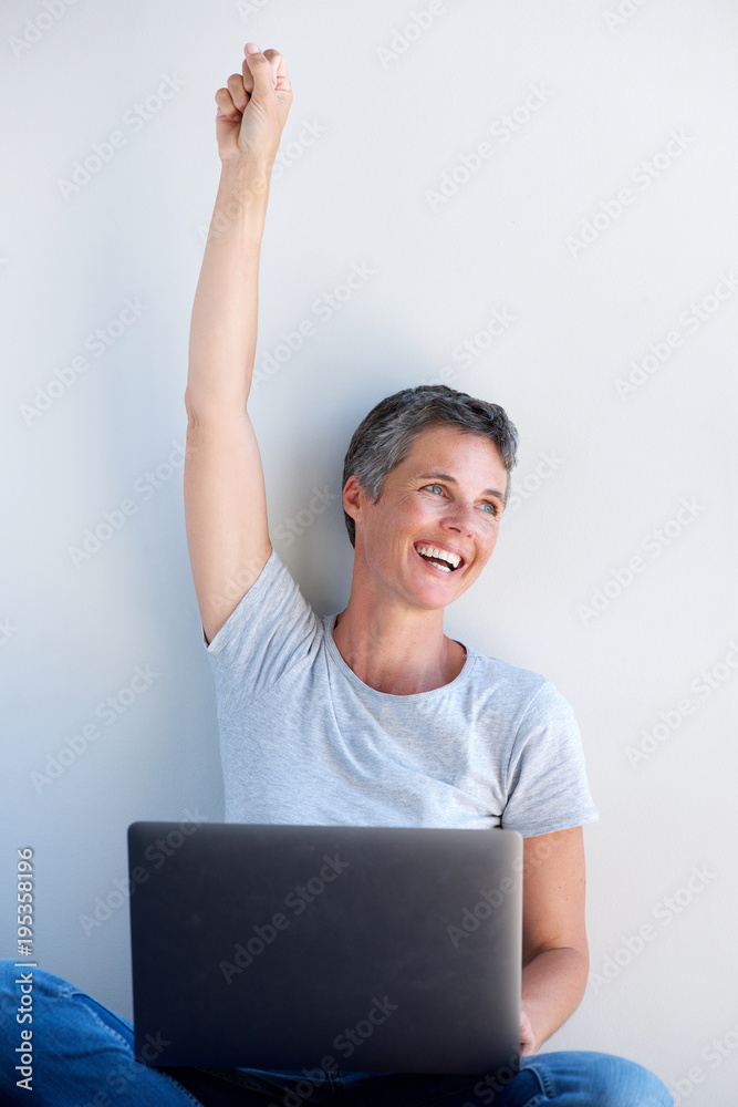 happy older woman using laptop with hand raised abasing white wall happy older woman using laptop with hand raised abasing white wall
