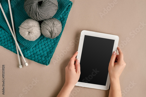 Grey and turquoise knitting wool, knitting needles and a tablet with a black screen on beige background. Top view. Copy space photo