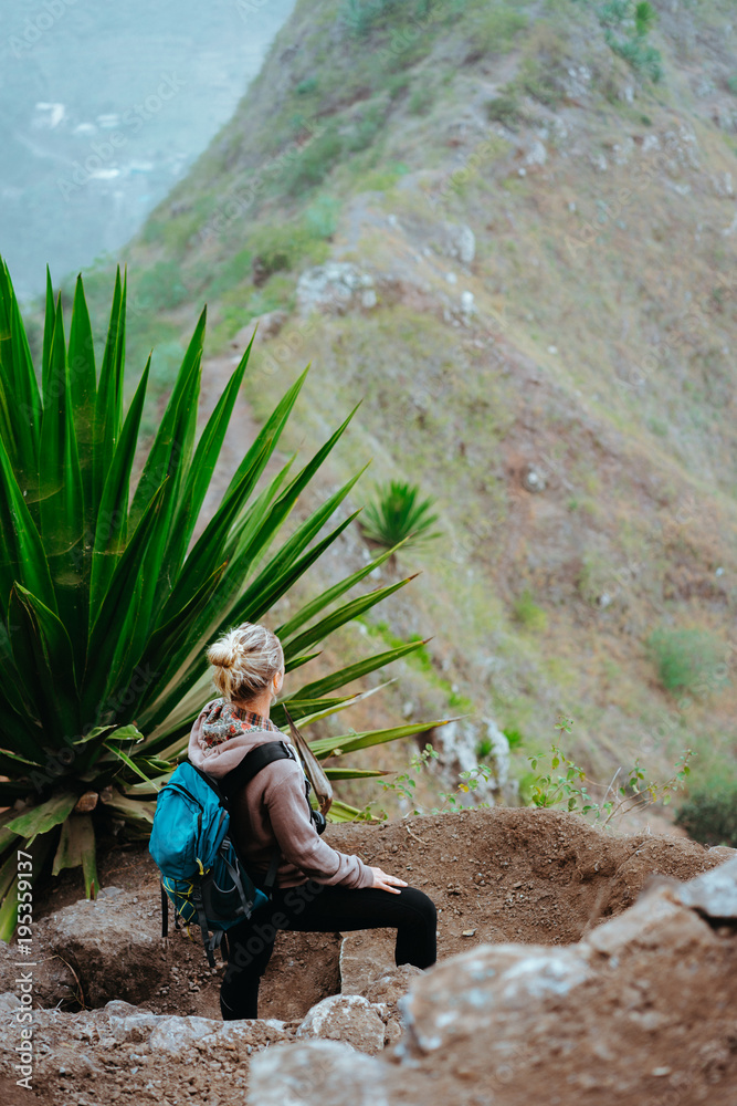 Woman with backpack on the trekking route near mountain edge looking down to valley. Santo Antao island, Cabo Verde