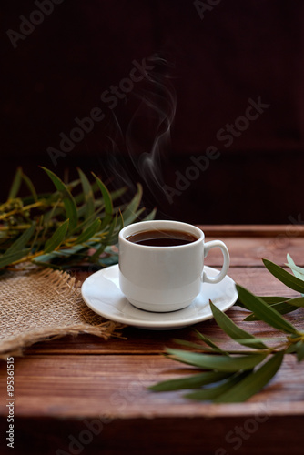 Чашка кофе с дымком, ветками эвкалипта, салфеткой из мешковины на деревянном коричневом фоне