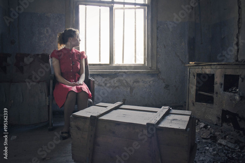 in an old wooden house, a girl in a red dress sits on a chair