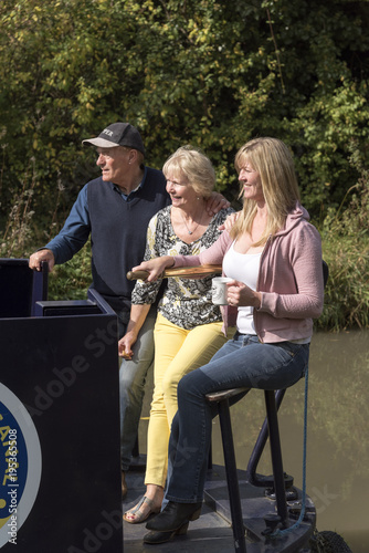 Fototapeta Holidaymakers standing on the stern of a holiday rental narrowboat enjoying tea