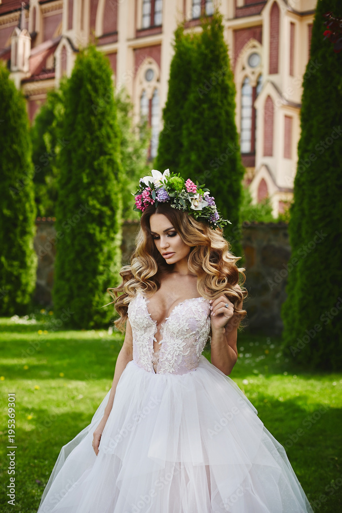 Very sexy and hot blonde model girl, in white dress and floral wreath on her head, is walking in front of church