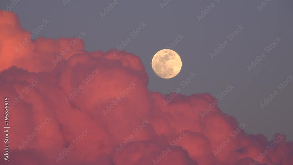 Full moon rising behind clouds illuminated by the sunset / time lapse