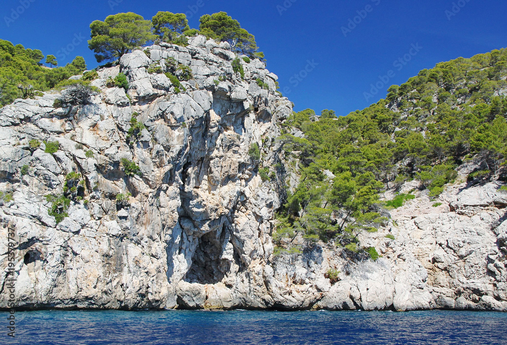 Beautiful cliff in Mediterranean sea covered with green trees. Blue sky background. Spain