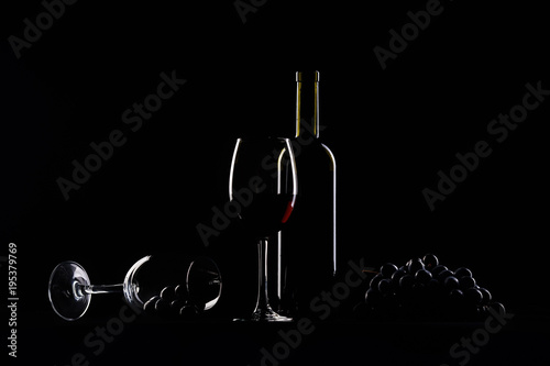 two glasses, bottle of wine and grapes on black background.
