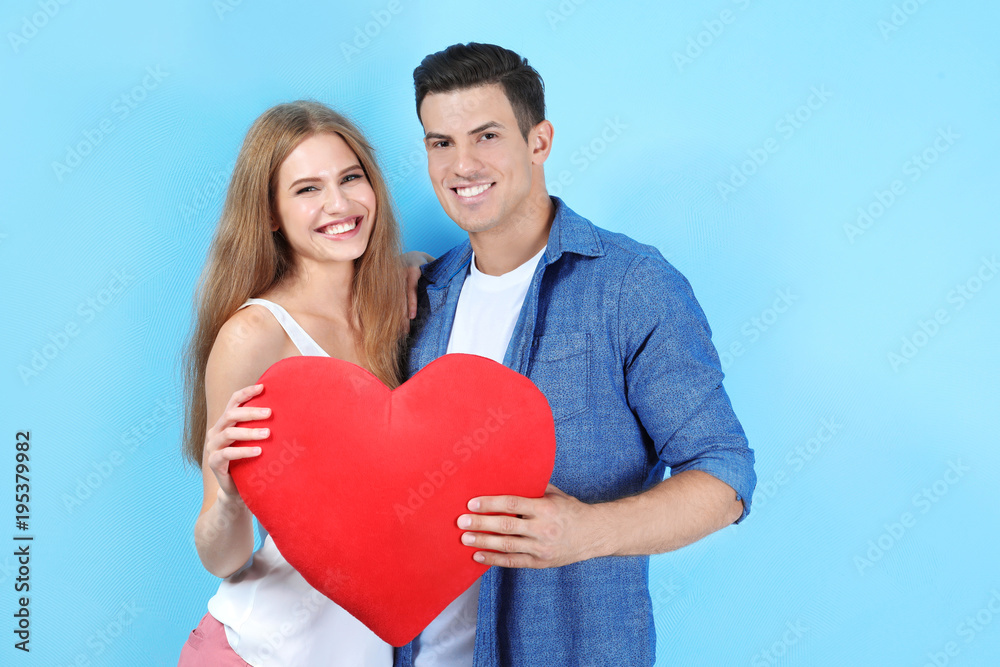 Young couple holding pillow in heart shape on light background