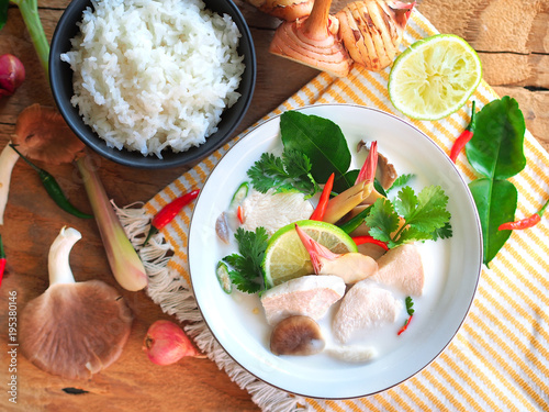 Thai galangal chicken soup in creamy coconut milk or Tom Kha Gai,famous traditional Thai food serve with jasmine steam rice in top view on wooden table background.