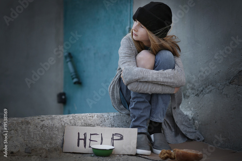 Slika na platnu Homeless poor teenage girl sitting outdoors near empty bowl and piece of cardboa