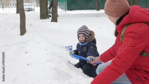 Cute little boy and young mother play in the winter with snow in the park. Blue kid's jacket and red at mom.