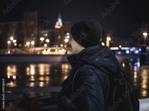 close up portrait of man in hat and jacket standing near the river in the night city