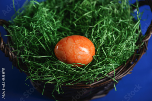 Painted Easter eggs of orange and light blue in green grass in a wicker basket.