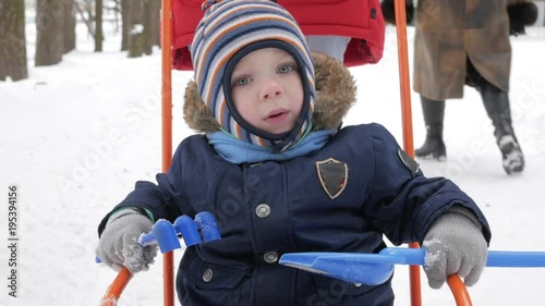 Cute little boy and young mother play in the winter with snow in the park. Blue kid's jacket and red at mom.