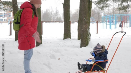 Cute little boy and young mother play in the winter with snow in the park. Blue kid's jacket and red at mom.