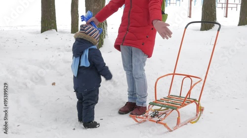 Cute little boy and young mother play in the winter with snow in the park. Blue kid's jacket and red at mom.