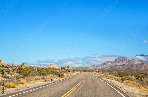A highway cutting through the Mojave desert with a large mountain in the foreground in a march landscape